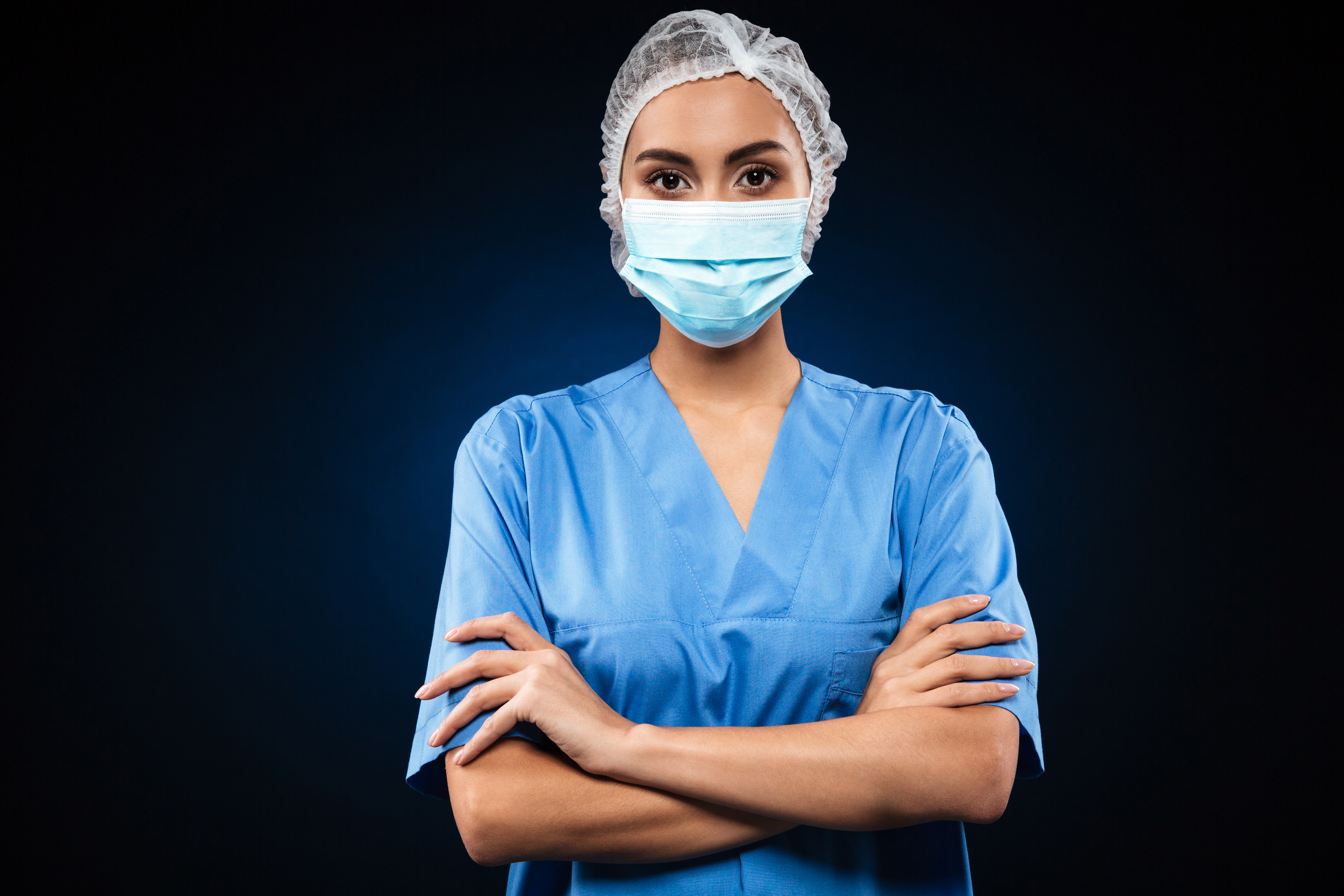 Serious doctor in medical mask and cap looking camera